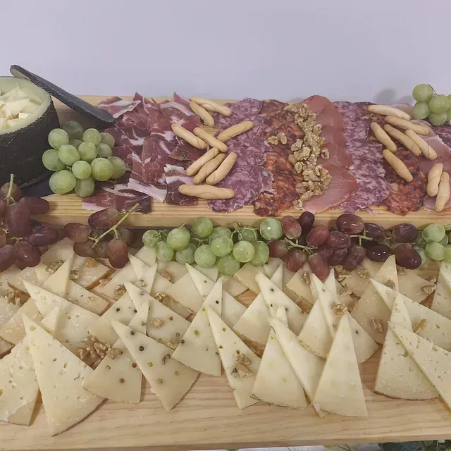 Una tabla de cortar de madera llena de queso, uvas y carne.