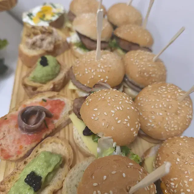 Una tabla de cortar de madera cubierta con hamburguesas y sándwiches en palillos de dientes.