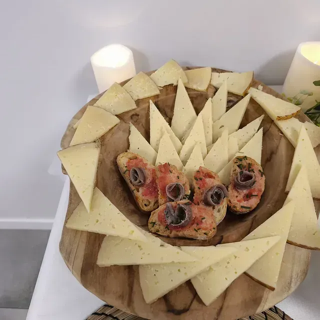 Un cuenco de madera lleno de rodajas de queso y aceitunas.