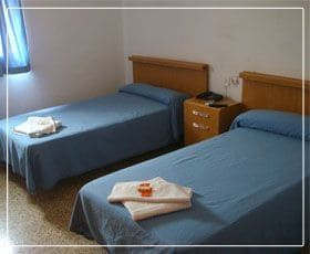 Dos camas individuales en una habitación con ropa de cama azul y una mesita de noche entre ellas.