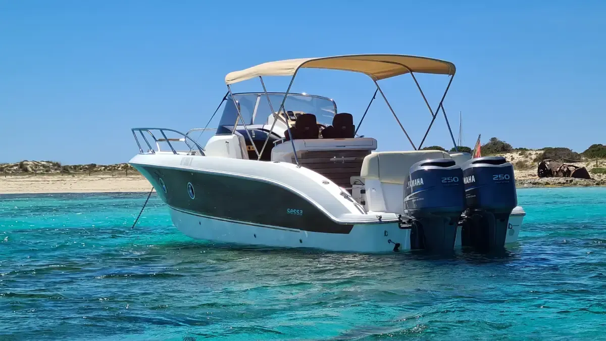 Lancha motora blanca con toldo color canela y dos motores fueraborda en aguas azules cristalinas cerca de la costa.