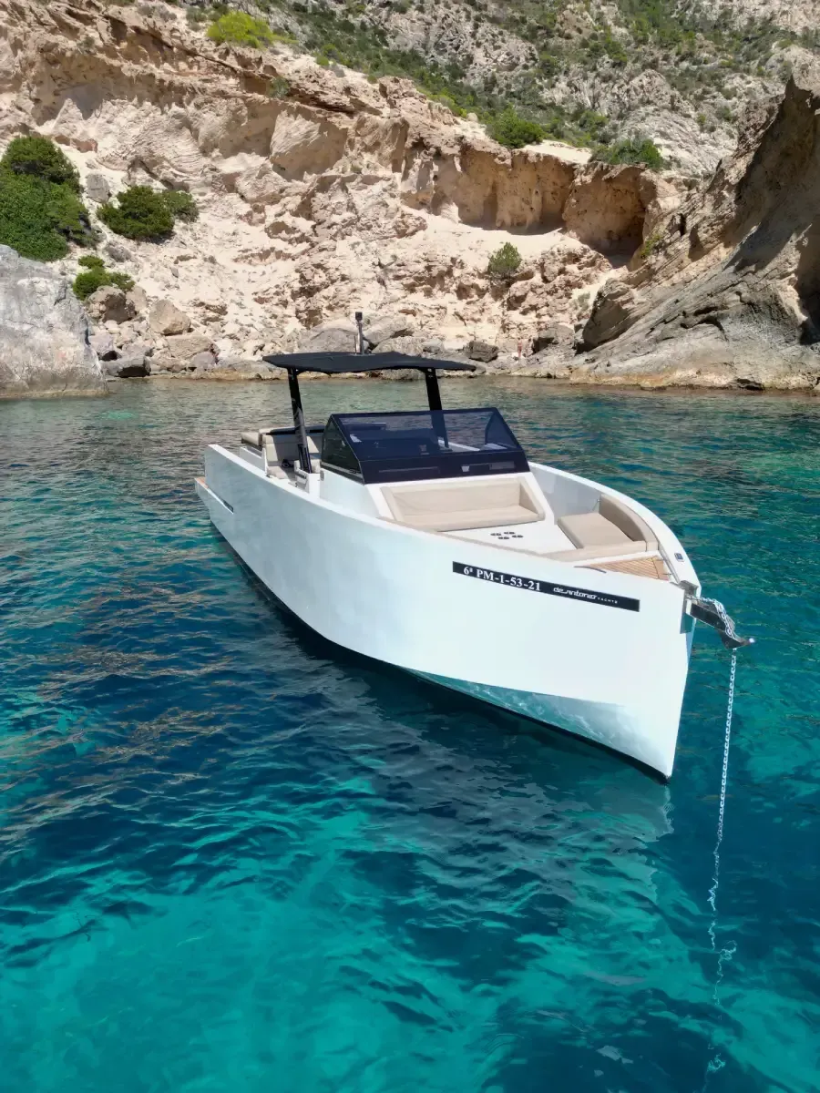 Lancha motora blanca flotando en aguas cristalinas de color turquesa cerca de un acantilado rocoso.
