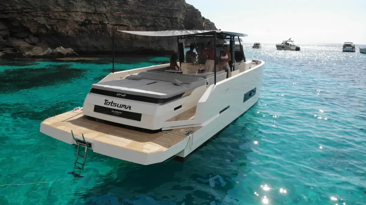 Yate de lujo a motor en aguas turquesas cerca de acantilados rocosos, con otros barcos en la distancia.