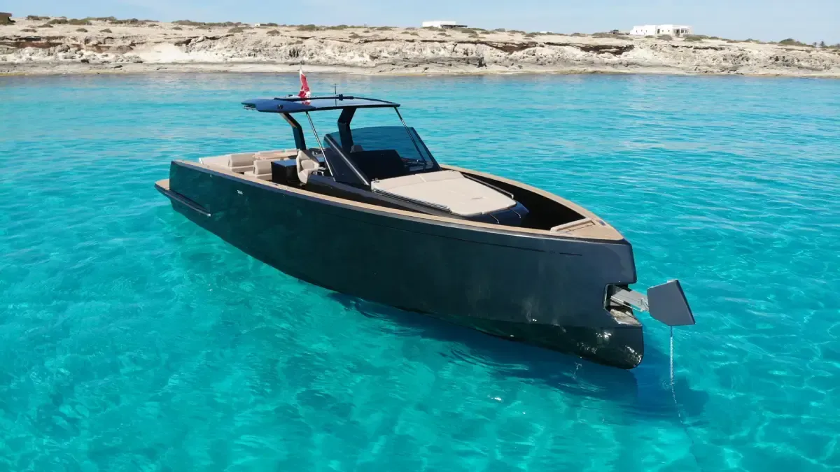 Lancha motora negra flotando sobre aguas de color turquesa brillante cerca de una costa rocosa.