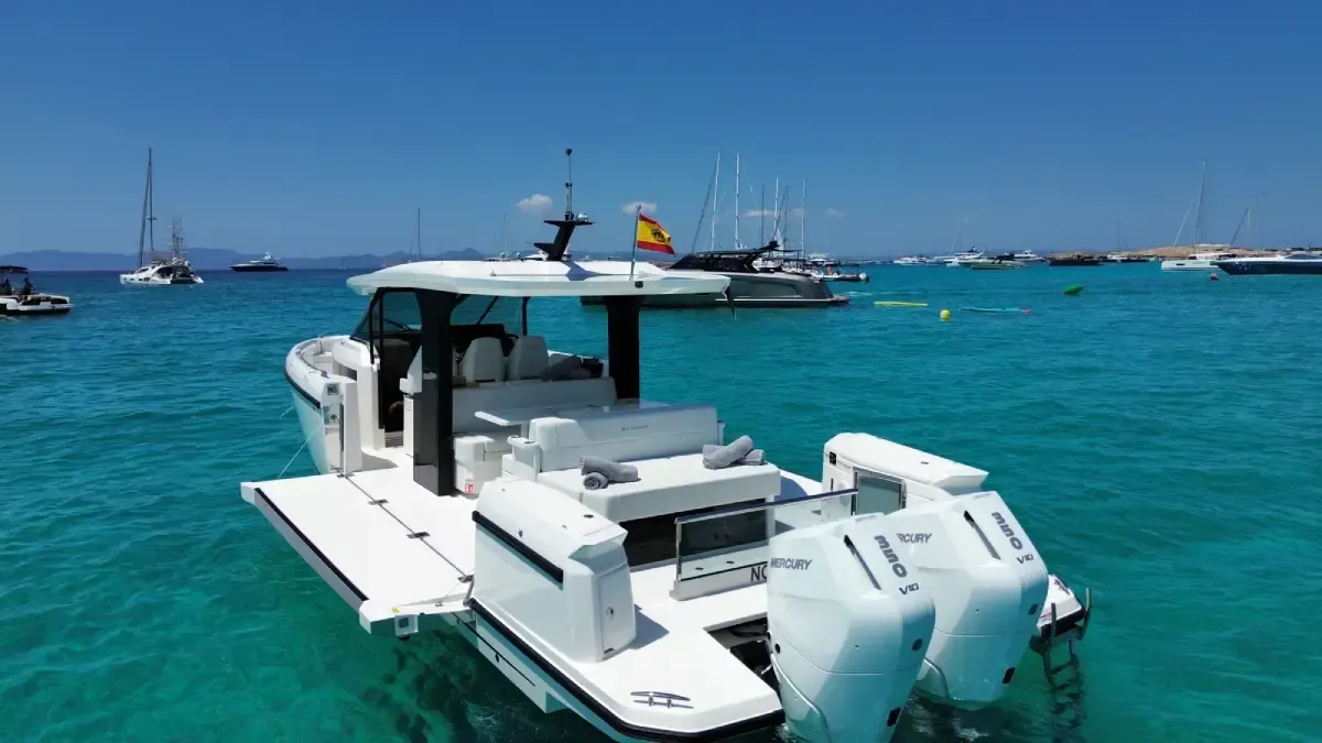 Un catamarán blanco en un mar turquesa con barcos anclados al fondo bajo un cielo azul claro.