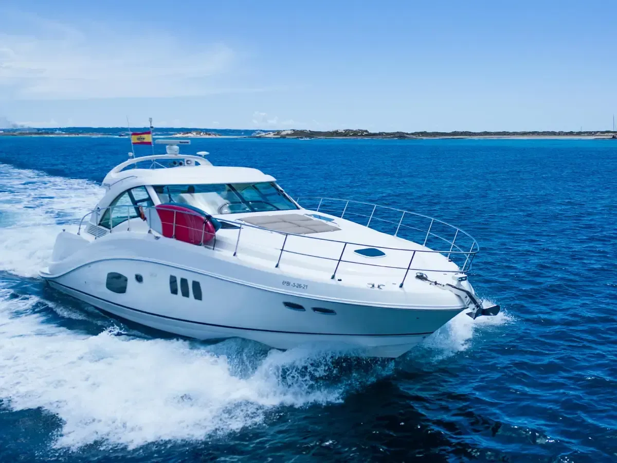 Yate blanco surcando a toda velocidad las aguas azules bajo un cielo despejado.