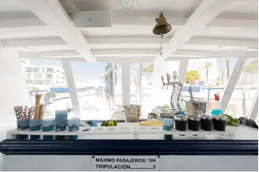 Estación de bebidas en la luminosa cubierta de un barco, con vasos, cepillos y botellas alineados sobre un mostrador.