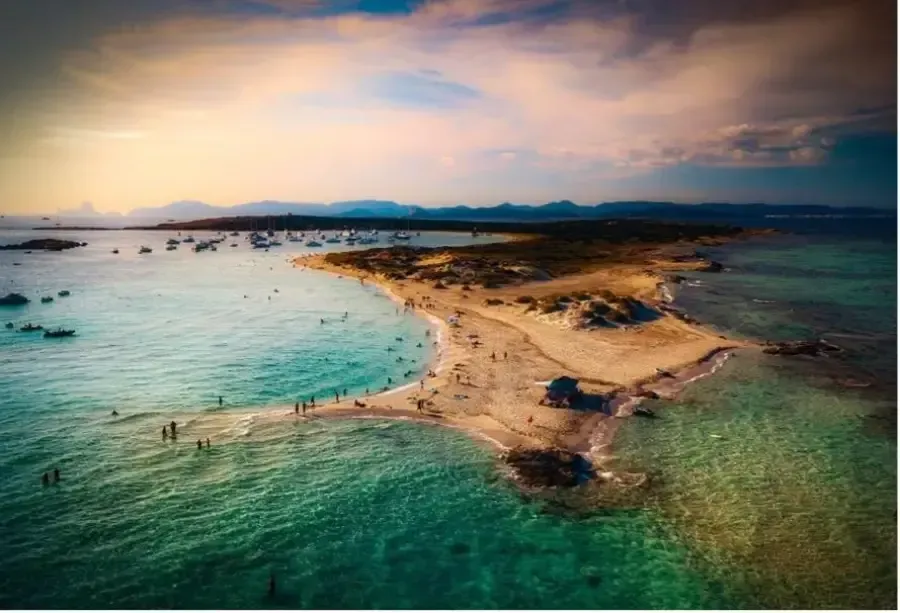 Vista aérea de una península arenosa en aguas turquesas bajo un cielo nublado al atardecer.