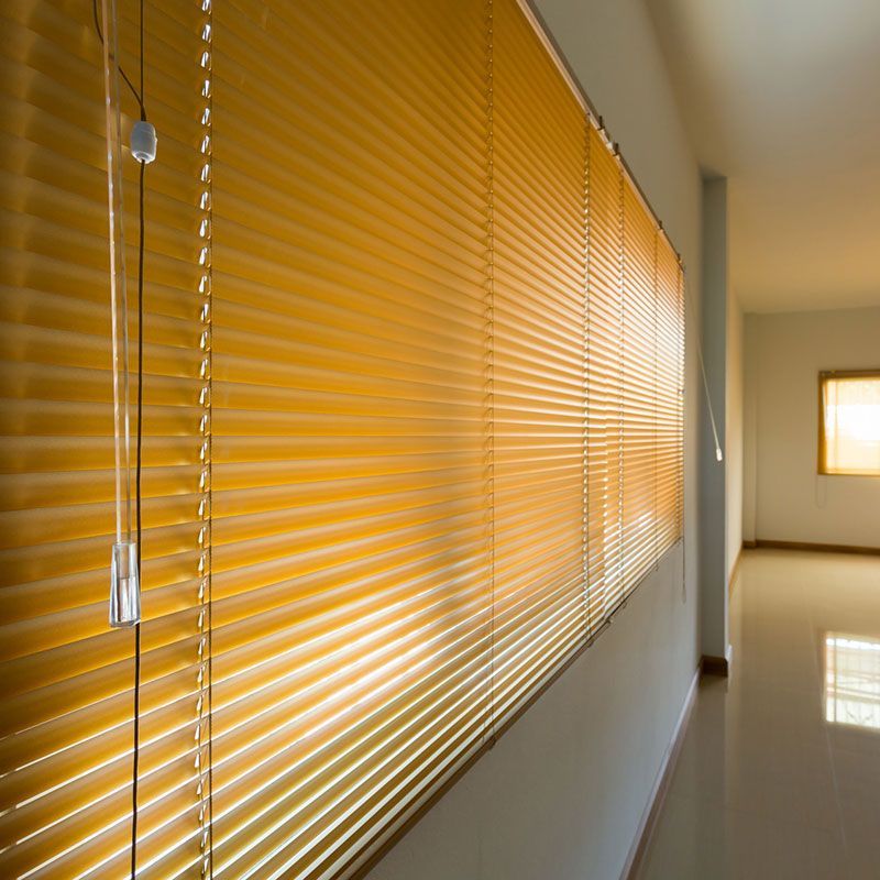 Ein langer Flur mit gelben Jalousien an den Fenstern