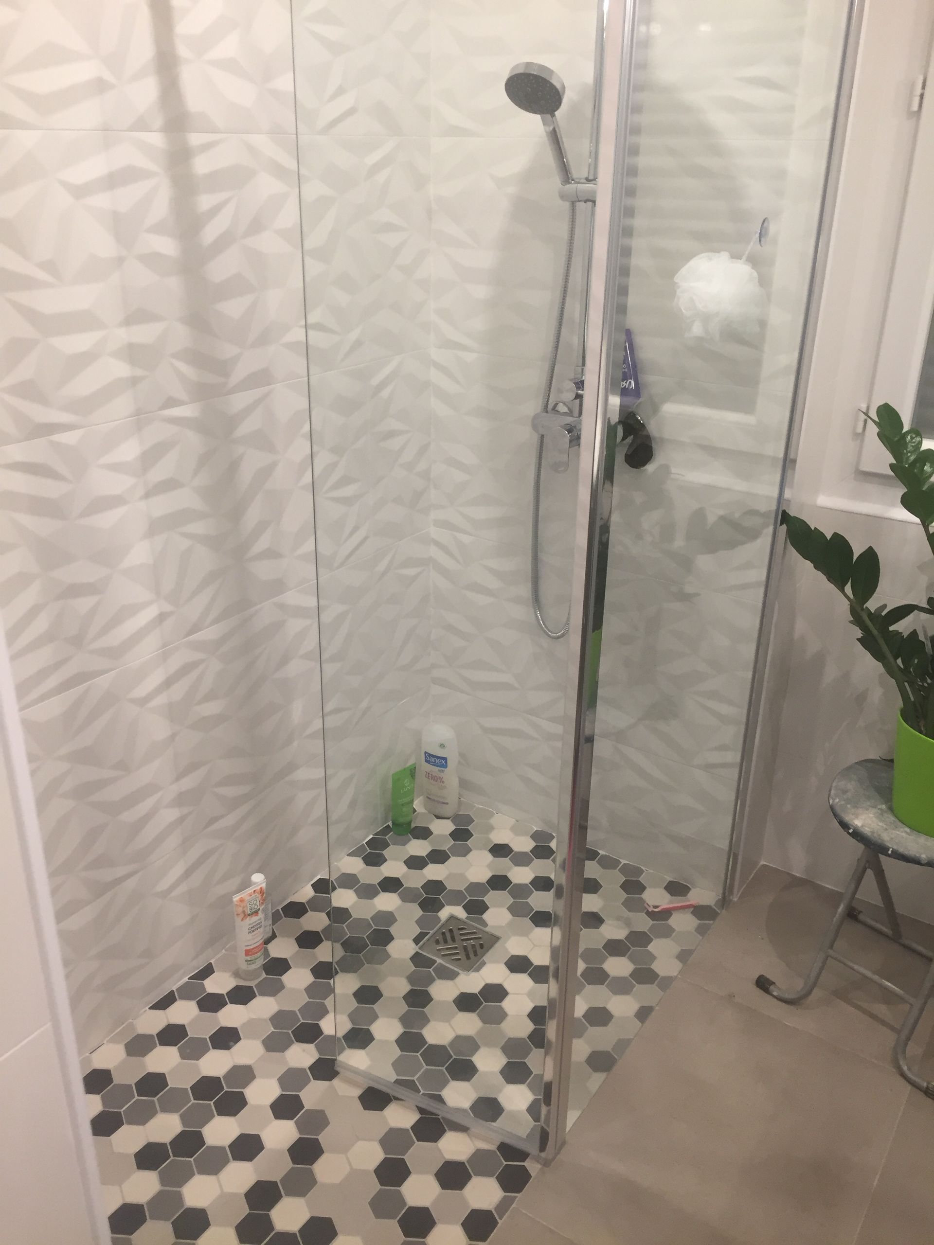 Douche avec carrelage mural blanc texturé et carrelage de sol hexagonal dans des tons de gris.