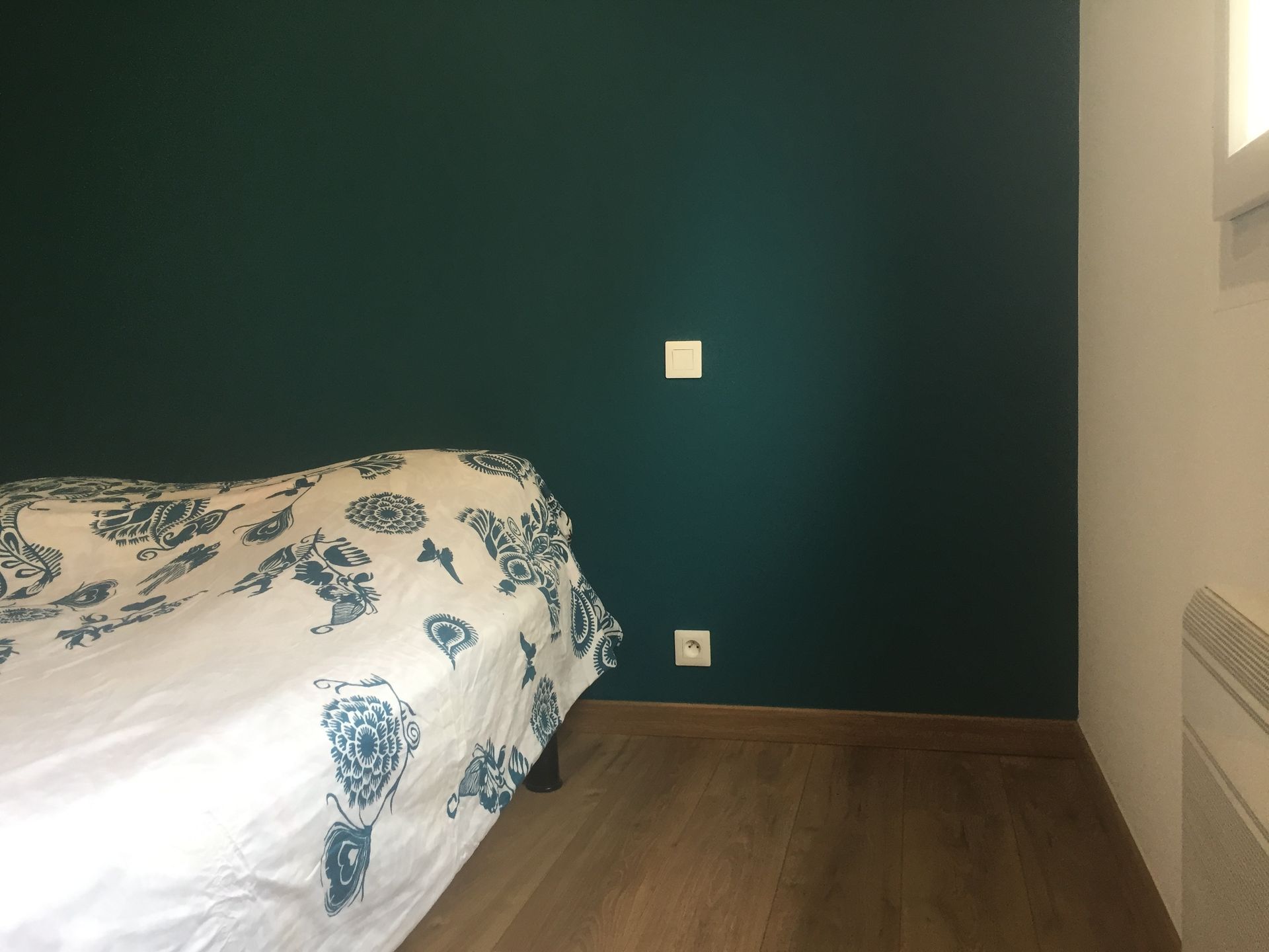 Chambre avec mur turquoise, lit avec linge de lit blanc à motifs, parquet et moulures blanches.