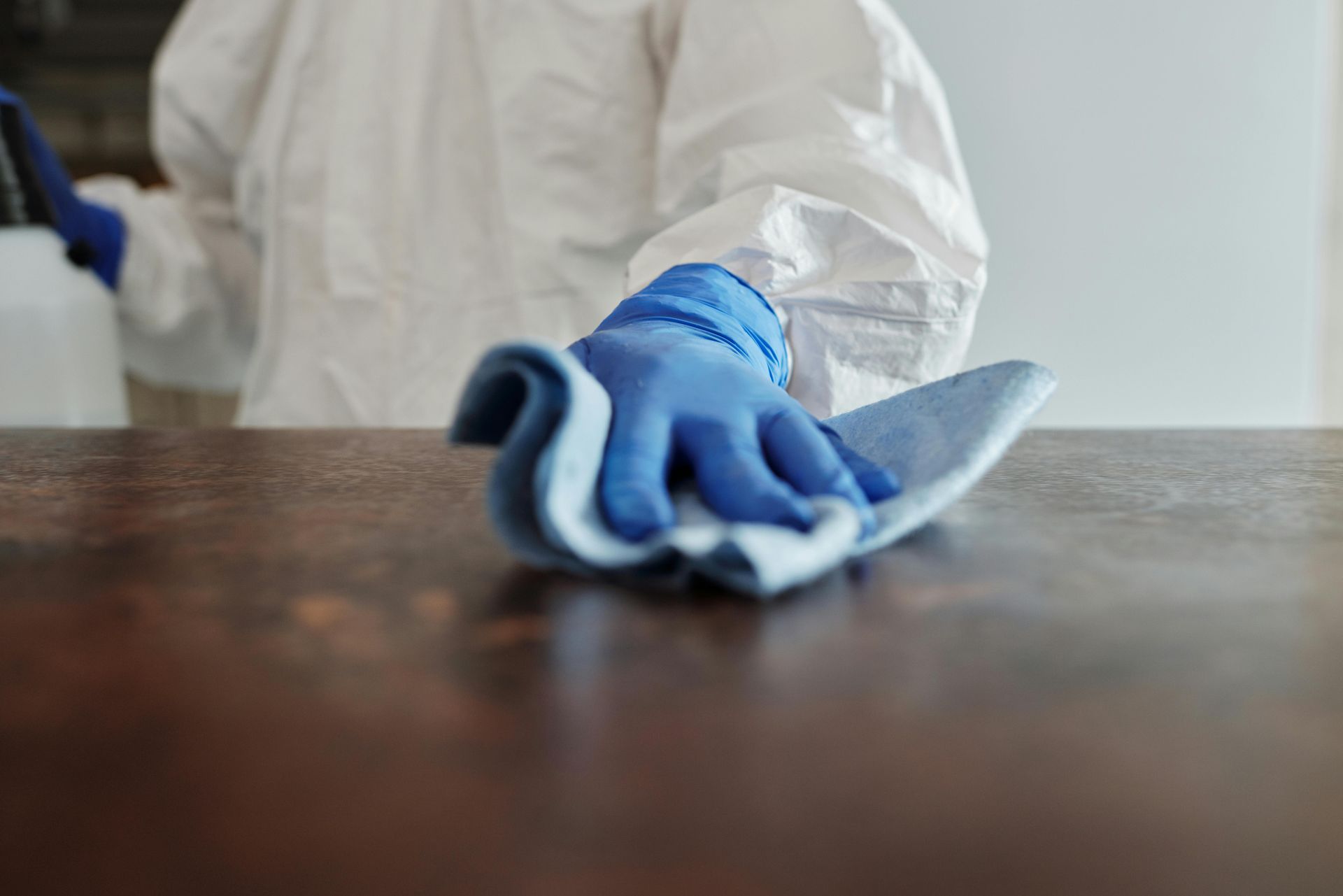 Person in Schutzkleidung reinigt eine braune Arbeitsplatte mit einem blauen Tuch.