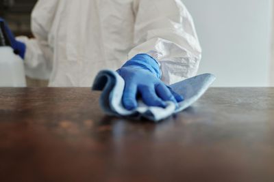Person in Schutzkleidung reinigt eine braune Arbeitsplatte mit einem blauen Tuch.