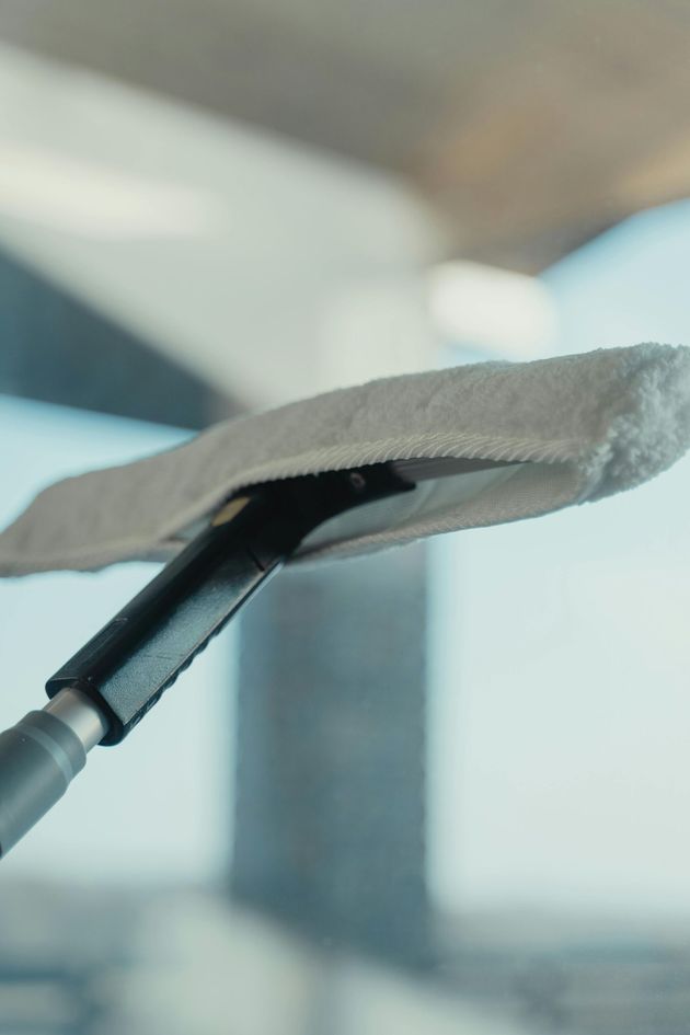 Fenster wird mit einem grau-weißen Reinigungswerkzeug gereinigt; heller Hintergrund.