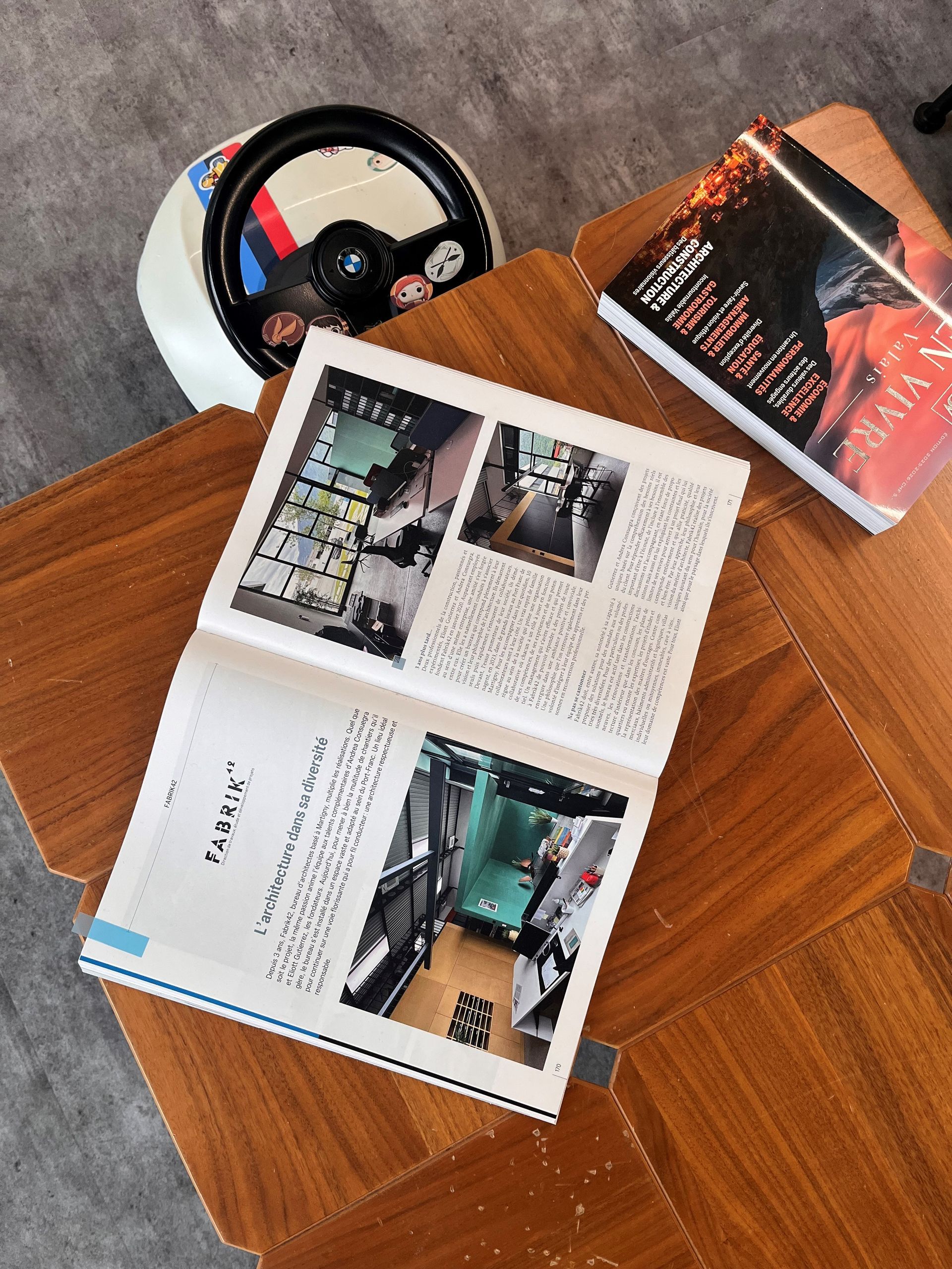 Un livre ouvert et un livre fermé sont posés sur une table en bois, à côté d'un objet blanc circulaire muni d'un volant noir.