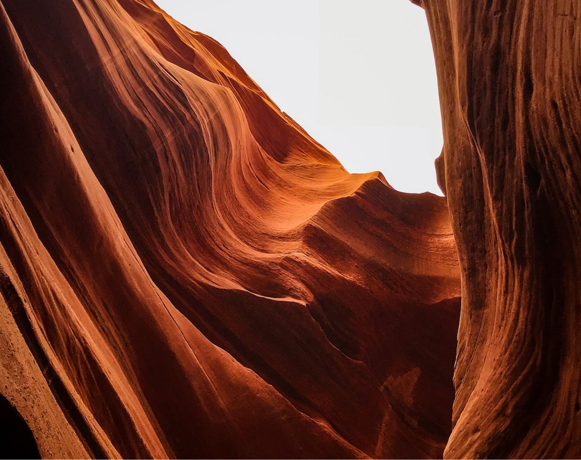 Vue plongeante sur les parois lisses et ondulées de grès orange d'un canyon étroit, avec un ciel lumineux visible au sommet
