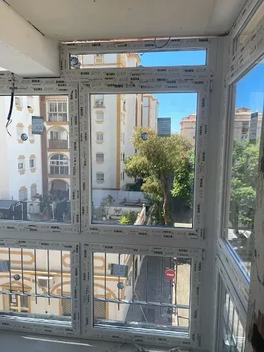 Vista a través de un gran ventanal de edificios de apartamentos y una calle arbolada en un día soleado