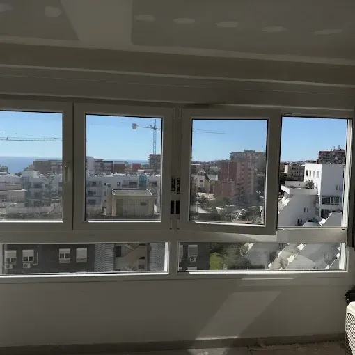 Vista desde una habitación a través de grandes ventanales, con vistas a una ciudad y al cielo azul