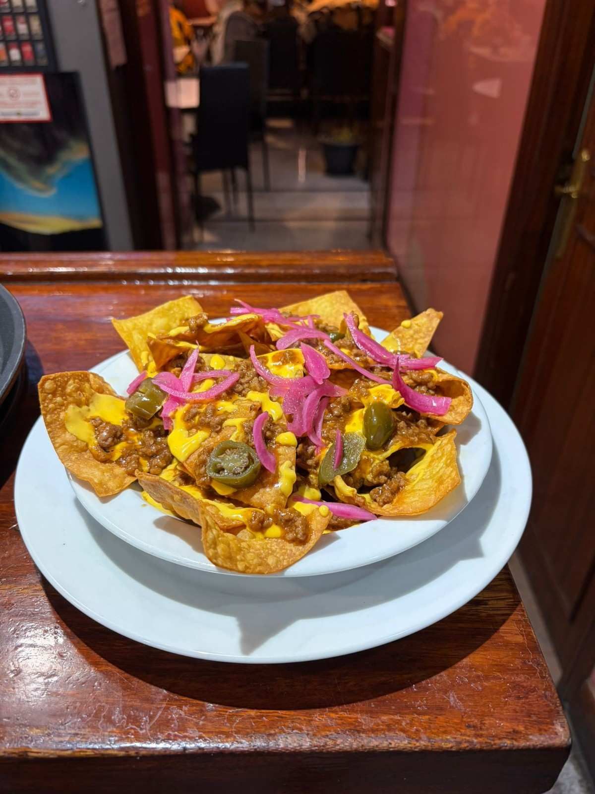Un plato blanco cubierto con una montaña de totopos dorados, queso fundido, carne picada, cebollas encurtidas y jalapeños.