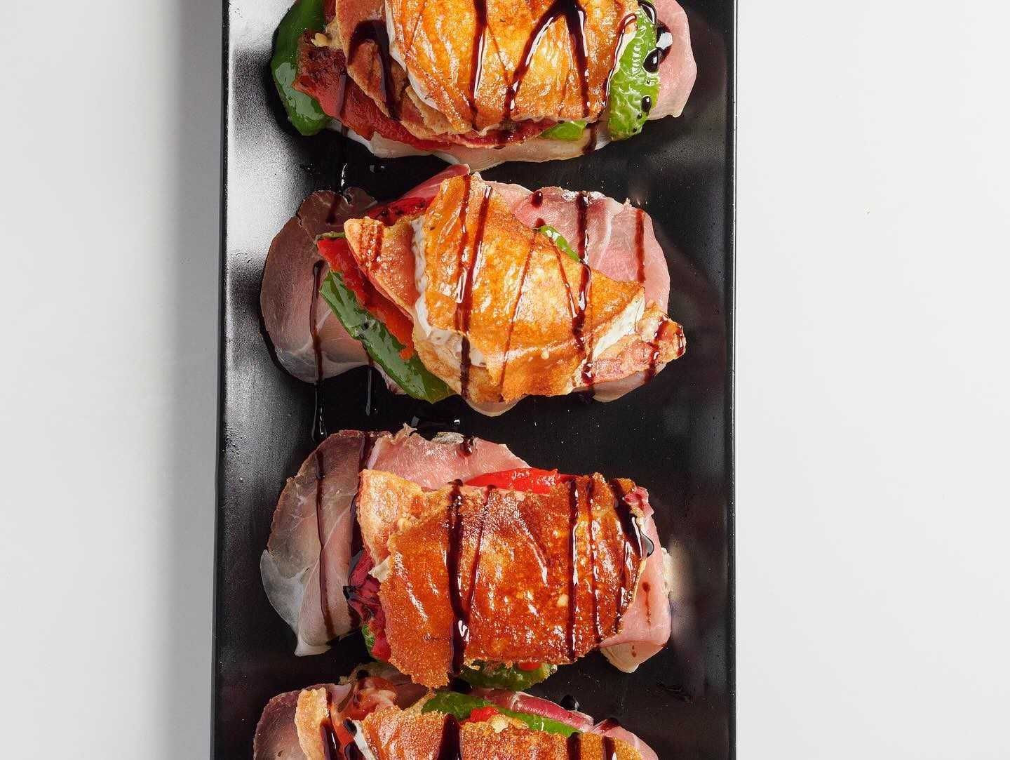 Cuatro pequeños sándwiches abiertos rociados con glaseado balsámico, servidos en un plato negro largo y rectangular.
