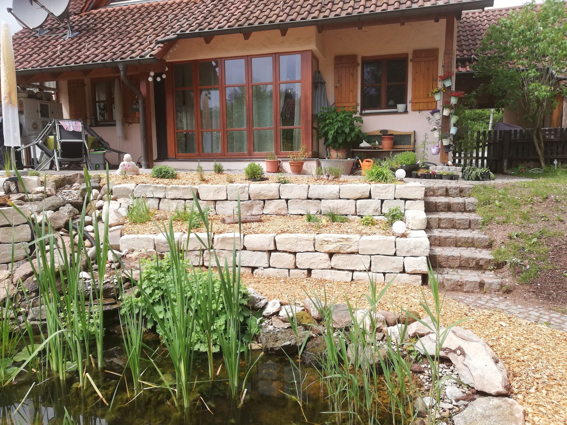 Vorgarten eines Hauses mit gepflastertem Weg, Steintreppen und Teich