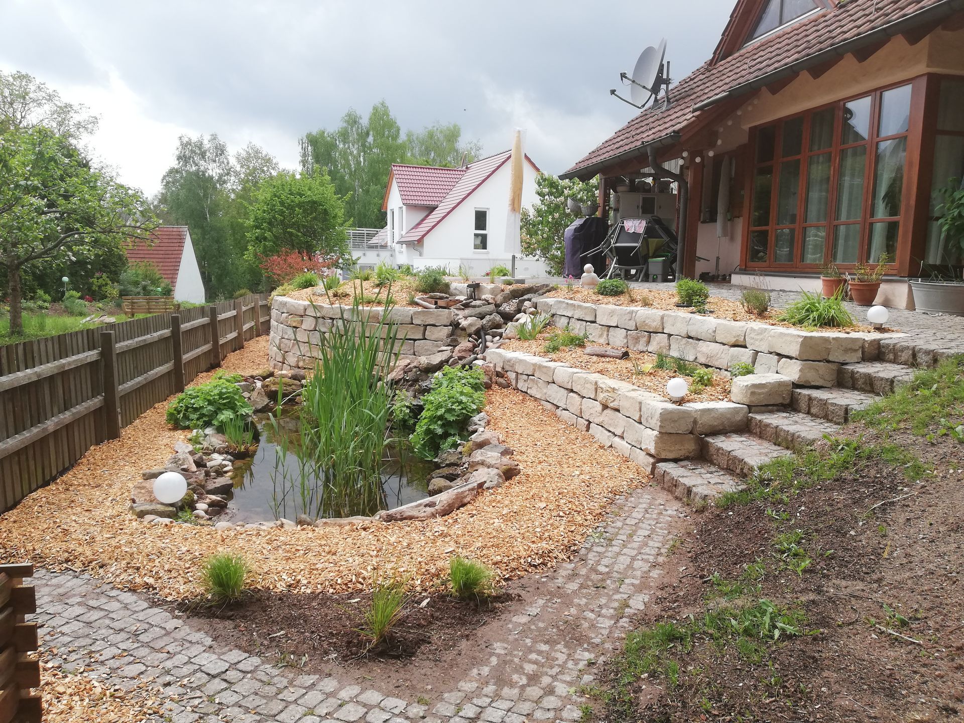 Vorgarten eines Hauses mit gepflastertem Weg, Steintreppen und Teich