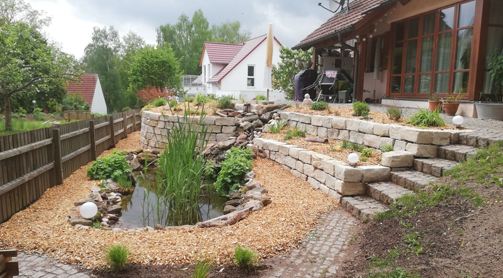 Vorgarten eines Hauses mit gepflastertem Weg, Steintreppen und Teich