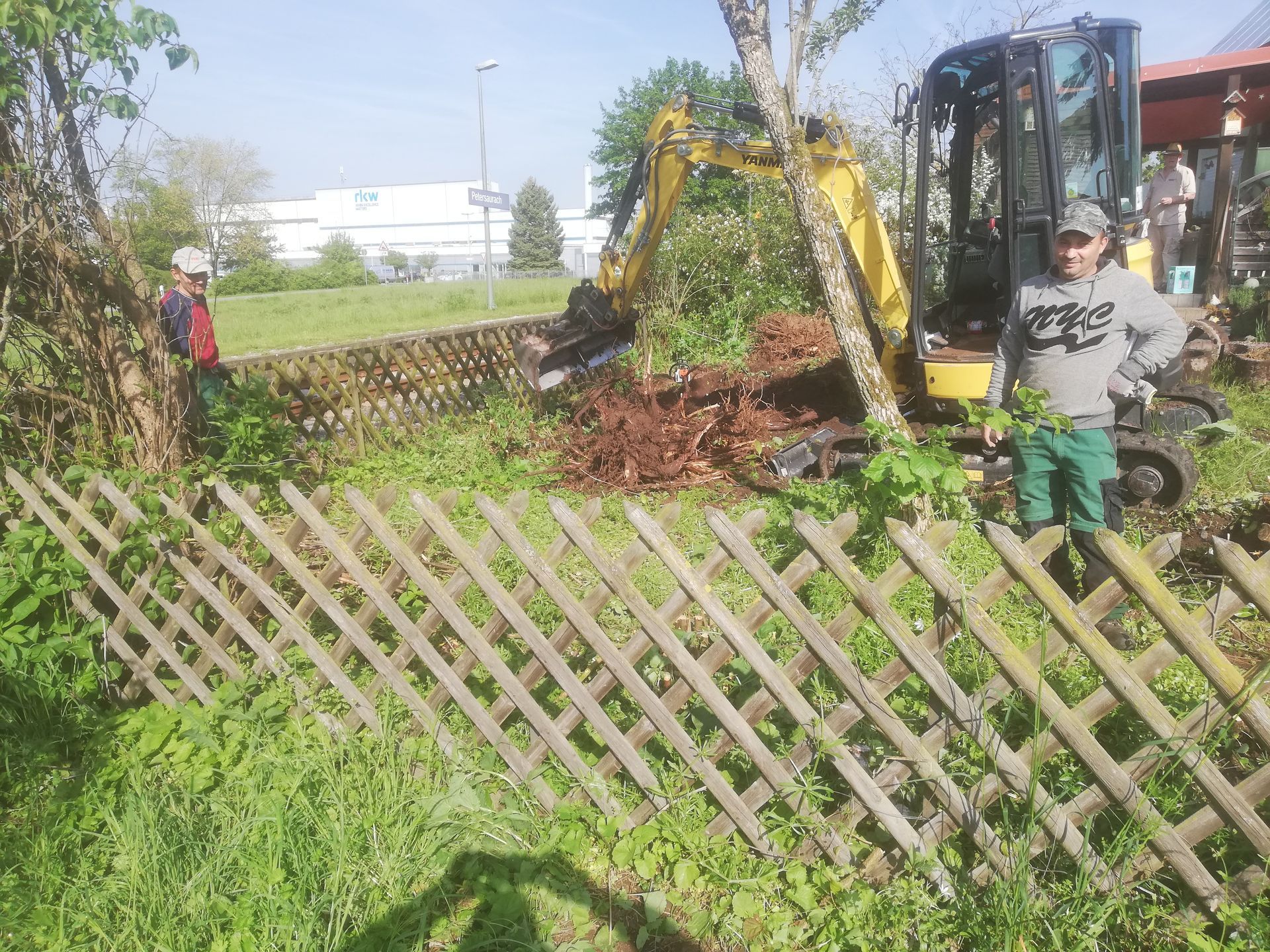 ein Mann mit einem gelben Bagger steht hinter einem Holzzaun