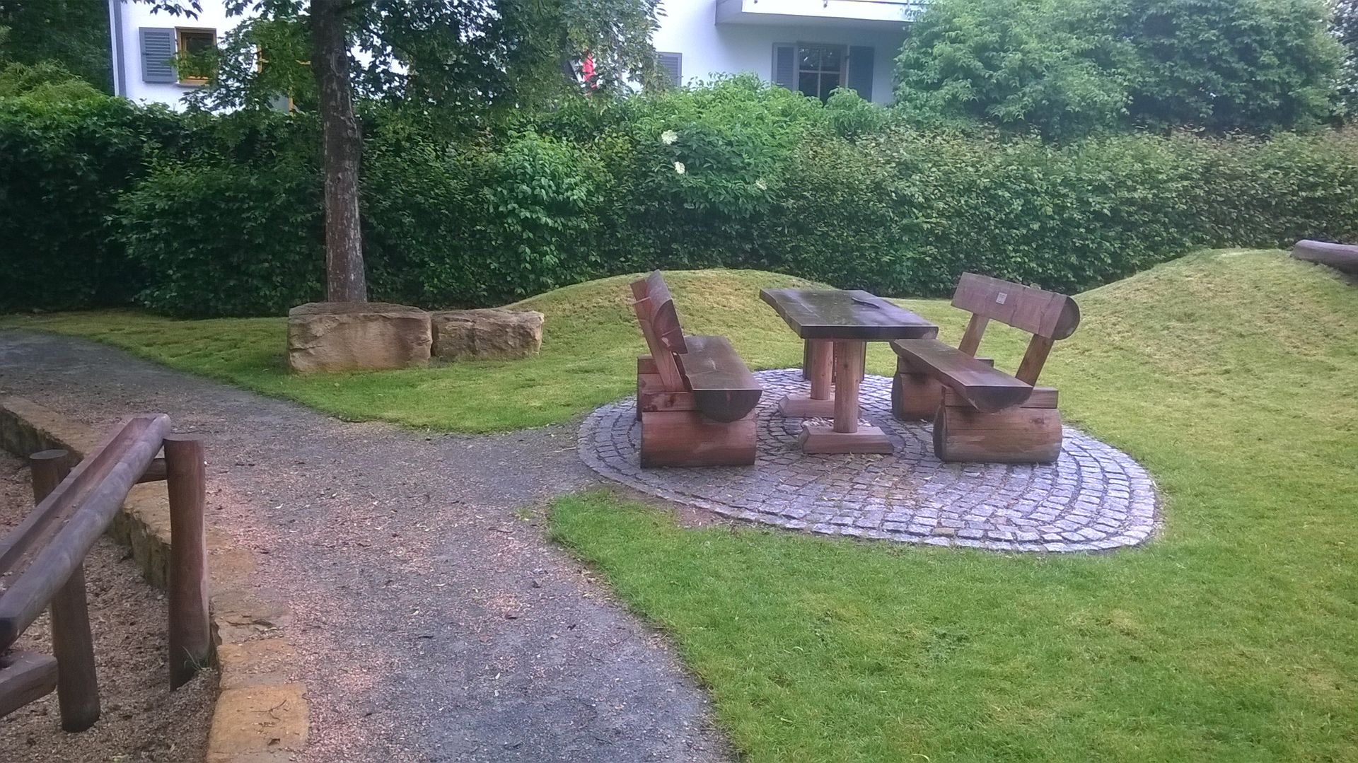 Bänke und Tisch aus Holz stehen auf einer runden gepflasterten Stelle in einem Park