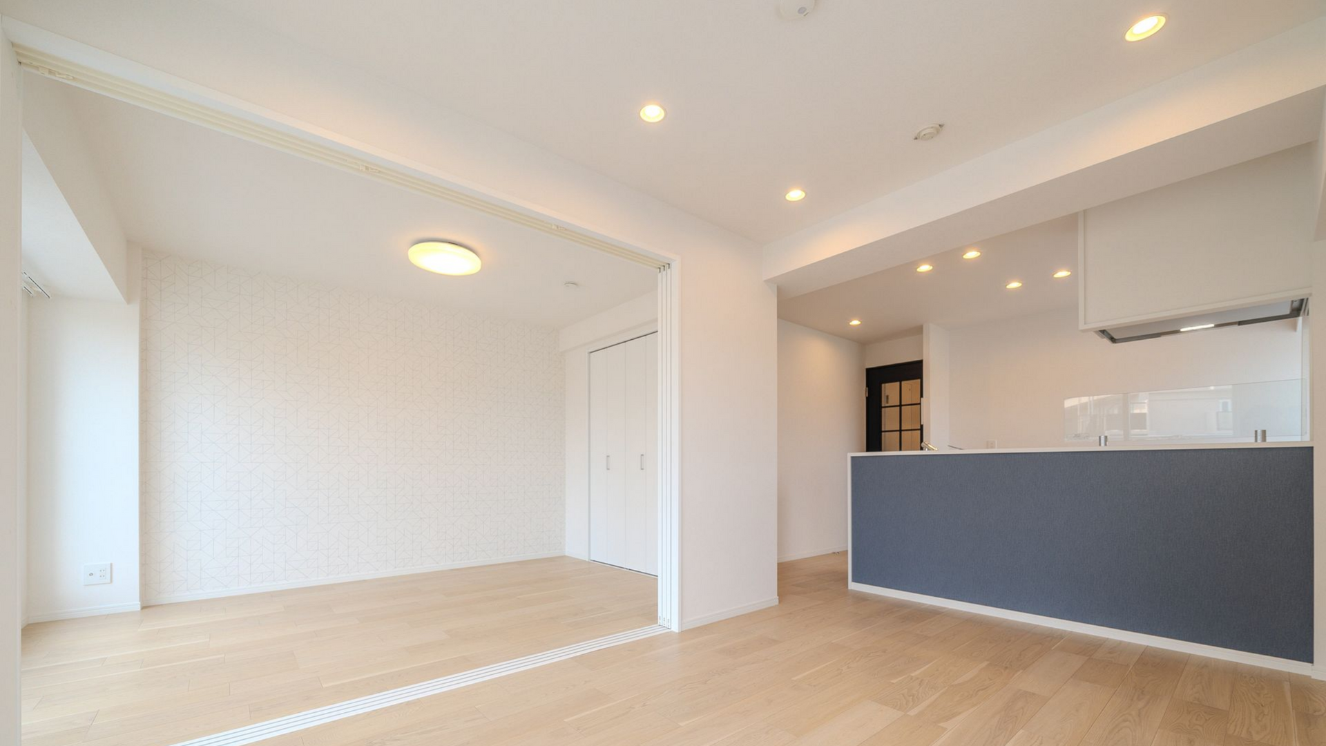 Intérieur d'un appartement moderne vide avec parquet clair, murs blancs et îlot de cuisine gris.