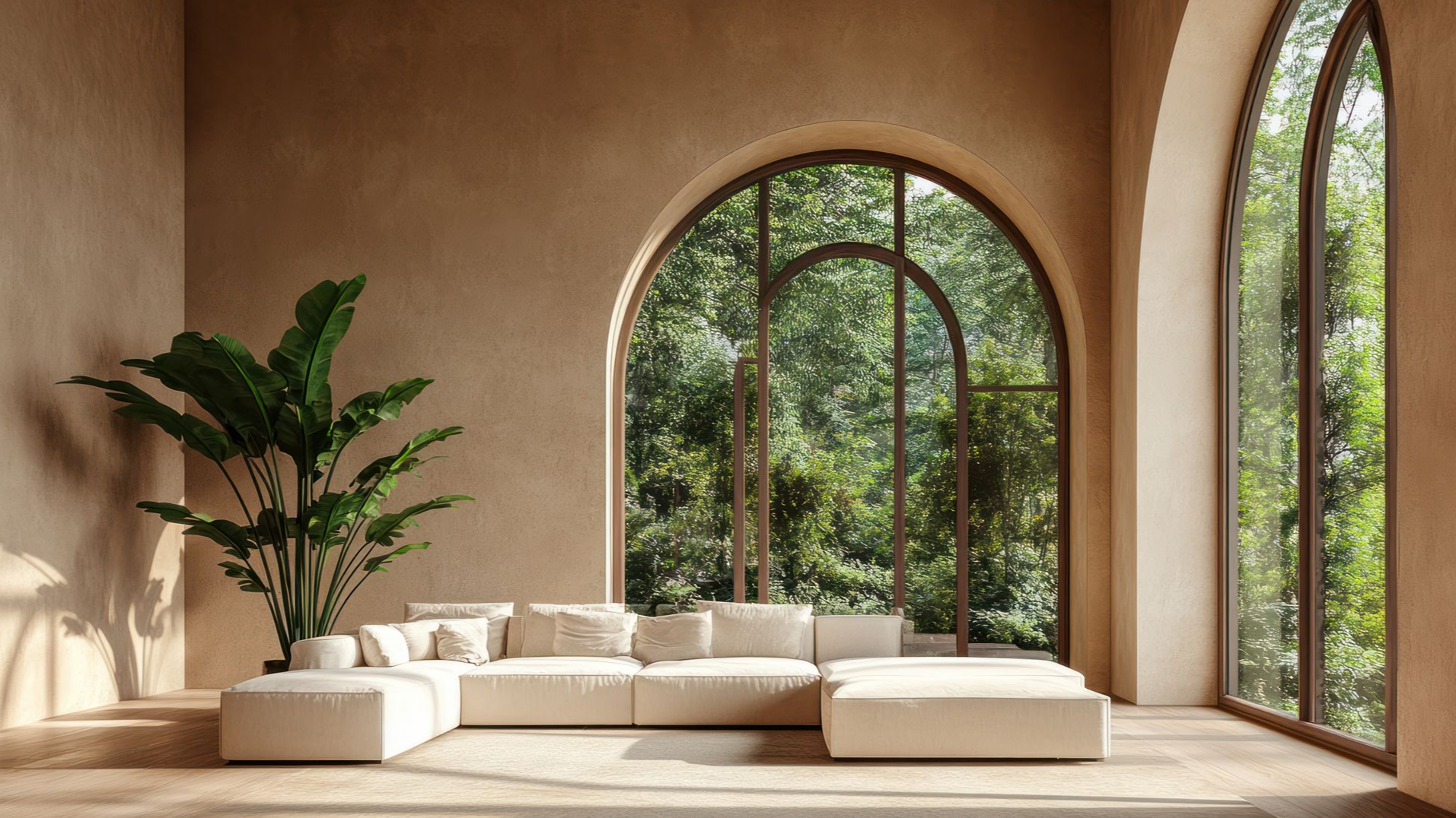 Salon beige avec fenêtres cintrées donnant sur une végétation luxuriante et un grand canapé d'angle.