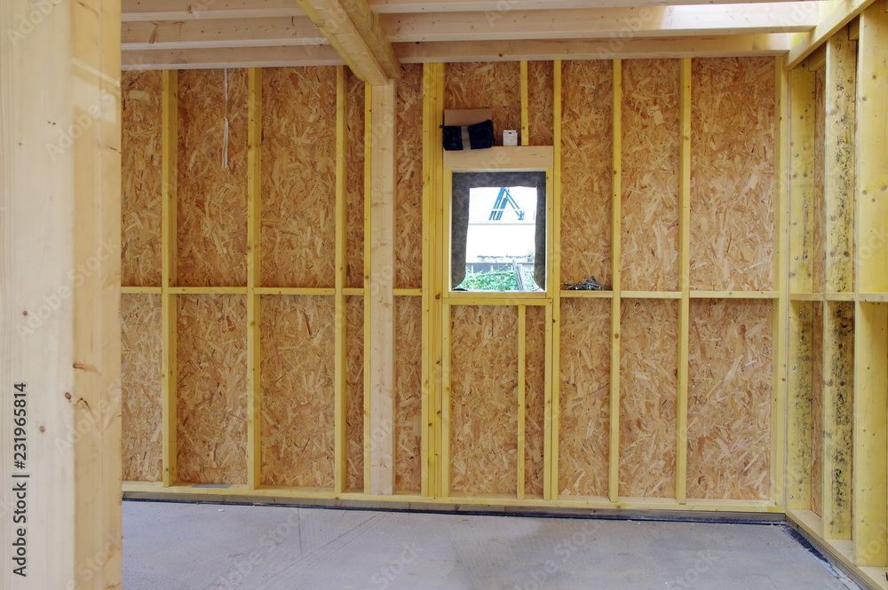 Vue intérieure d'un bâtiment en construction, montrant une ossature en bois, des murs en panneaux OSB et une petite fenêtre.