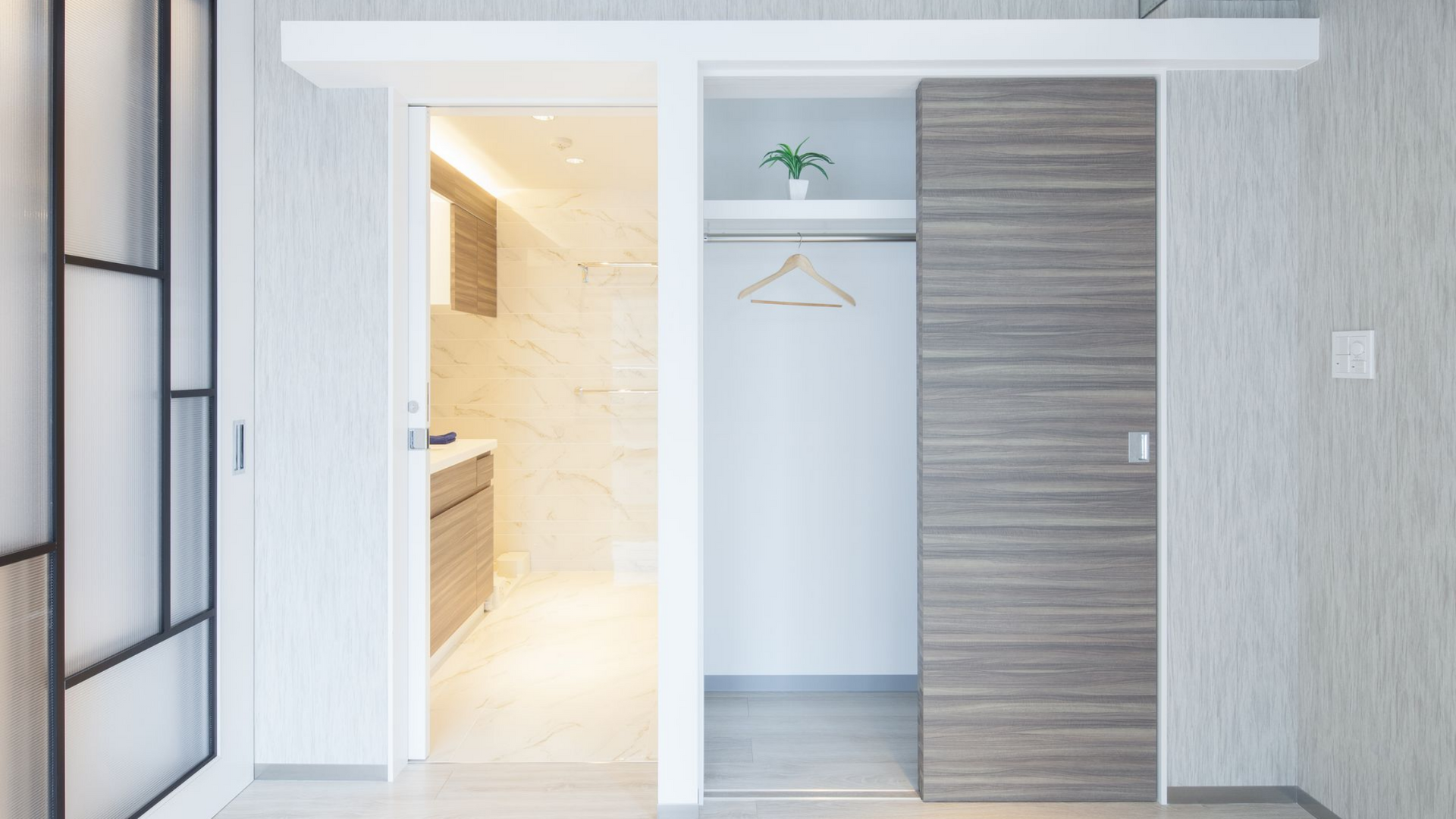 Intérieur d'appartement moderne avec portes coulissantes donnant sur le dressing et la salle de bains. Tons neutres et design minimaliste.