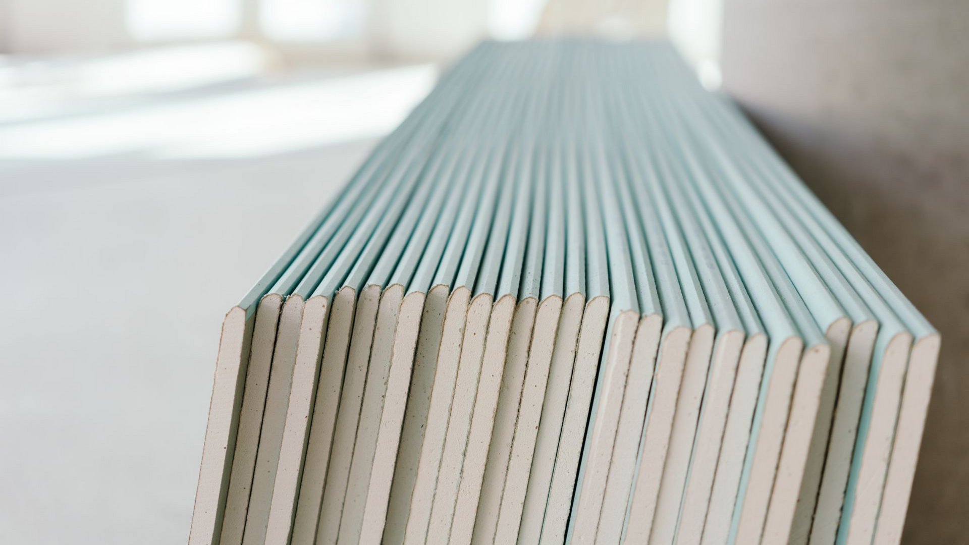Pile de plaques de plâtre recouvertes de papier bleu-gris, appuyées contre un mur sur un chantier de construction.