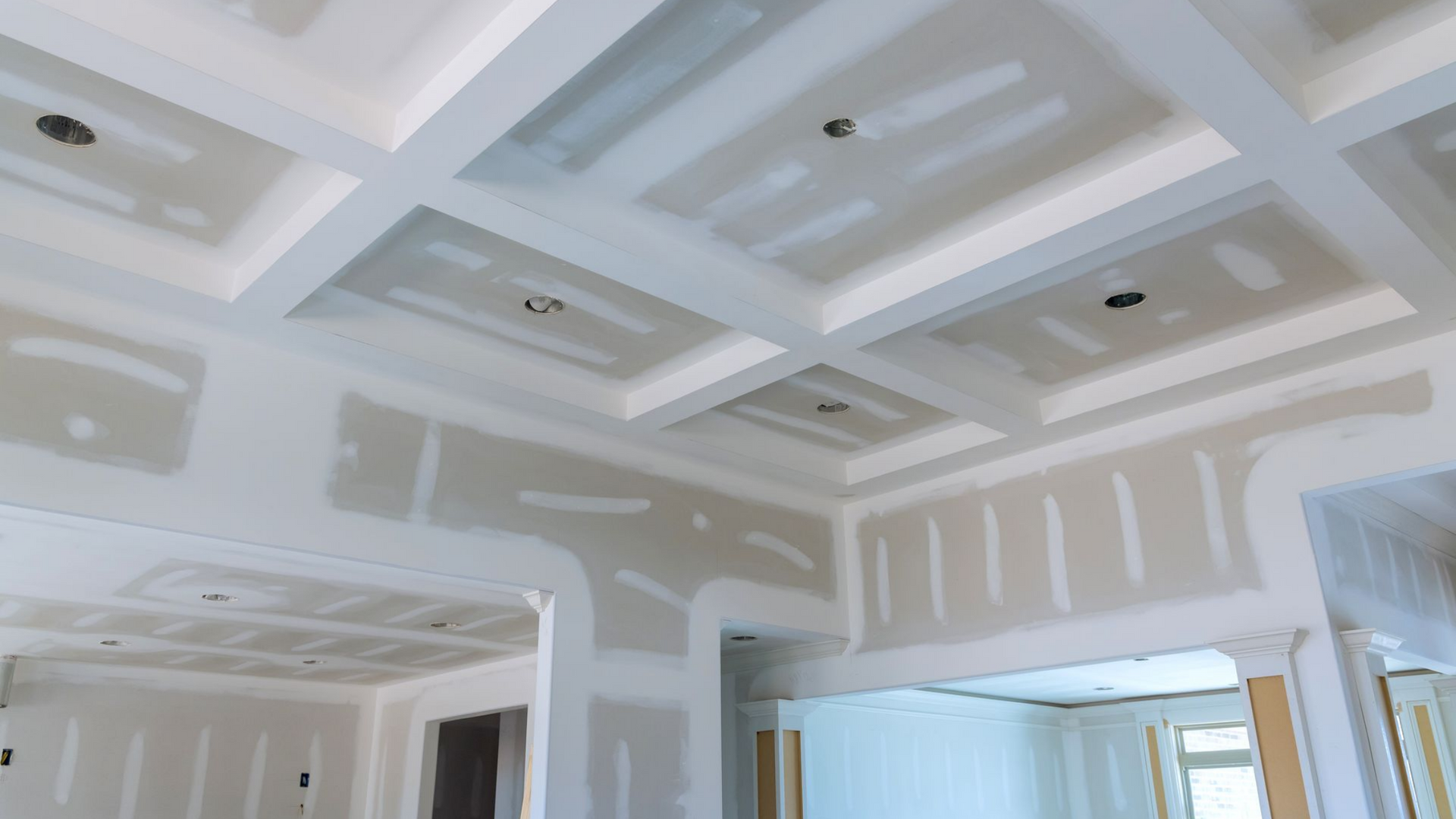 Travaux de construction intérieure en cours, pose de plaques de plâtre blanches au plafond et aux murs.