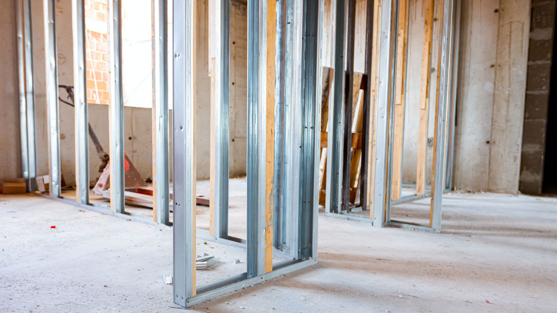 Vue intérieure d'une pièce en construction, avec des montants métalliques et en bois formant les murs, sur un sol en béton.
