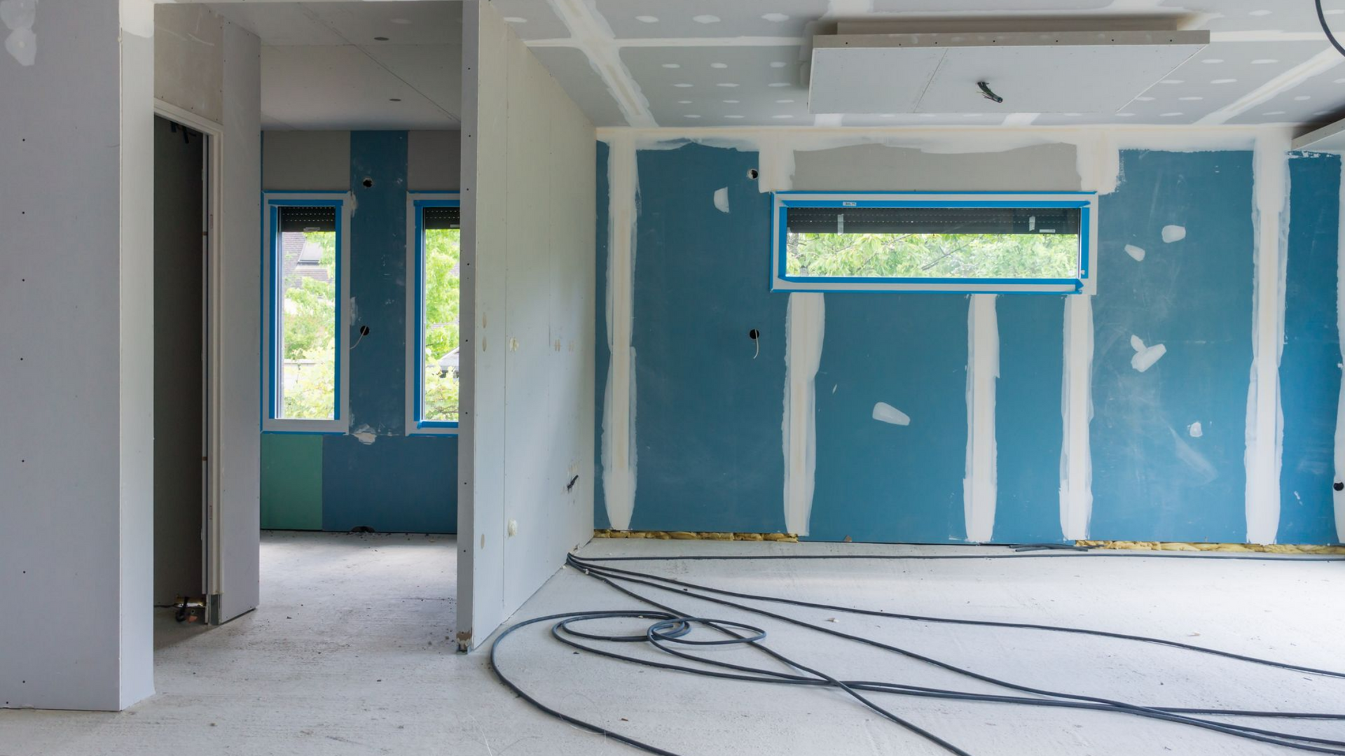 Intérieur d'une pièce en construction, avec des cloisons sèches bleues et une fenêtre.