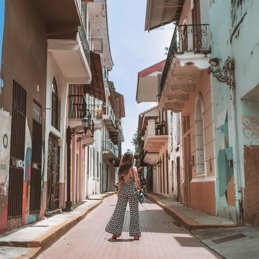 Una mujer camina por una calle estrecha entre dos edificios.