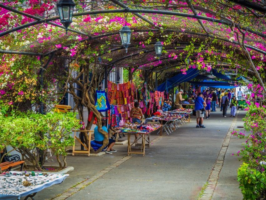 Un grupo de personas camina por una acera bajo un dosel de flores rosas.