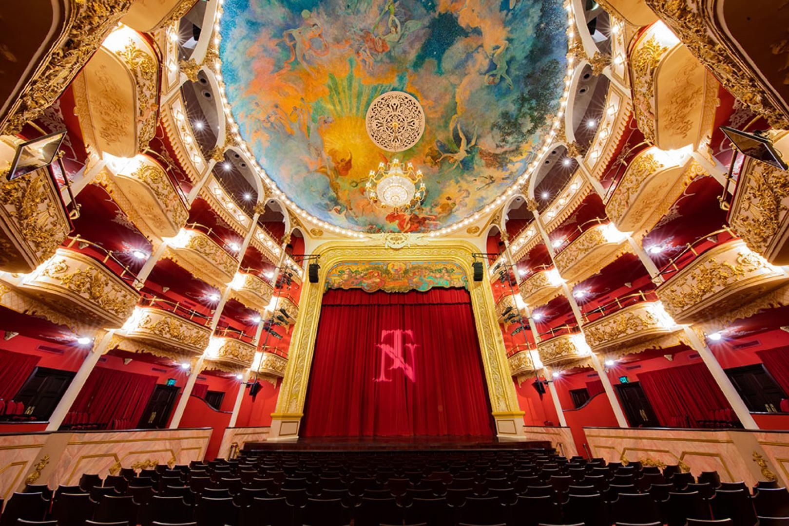 Un gran teatro vacío con una cortina roja y una pintura en el techo.