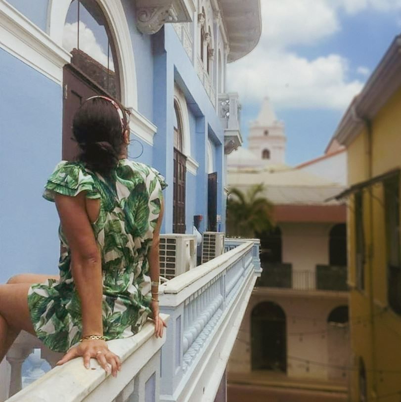Una mujer con un vestido verde está sentada en un balcón.