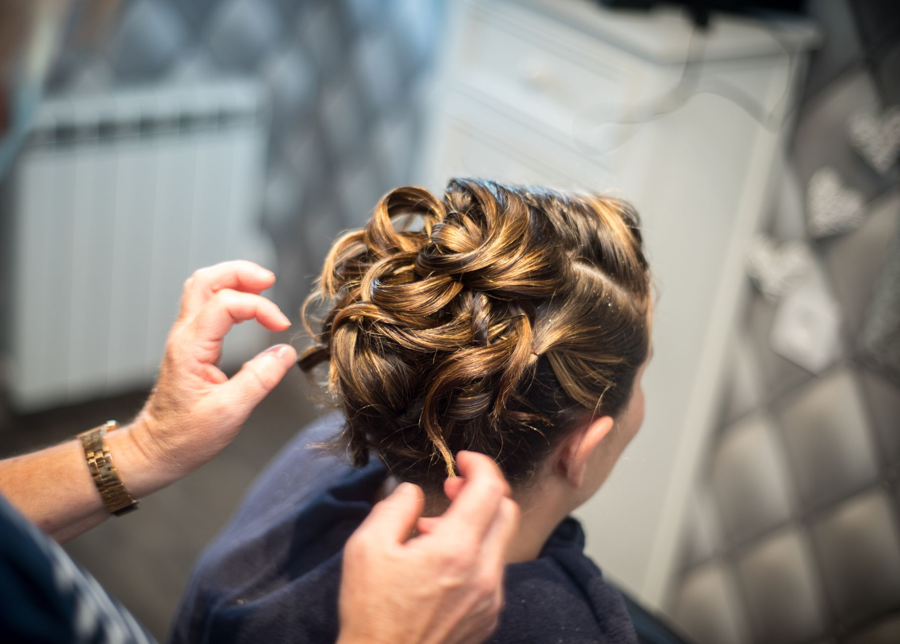 Mains coiffant une coiffure bouclée en chignon sur un fauteuil de salon