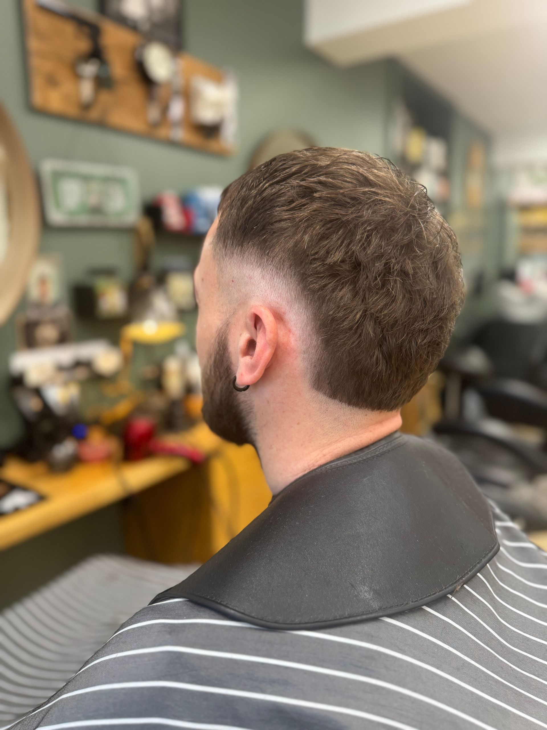 Un homme assis sur un fauteuil de barbier, arborant une coupe dégradée