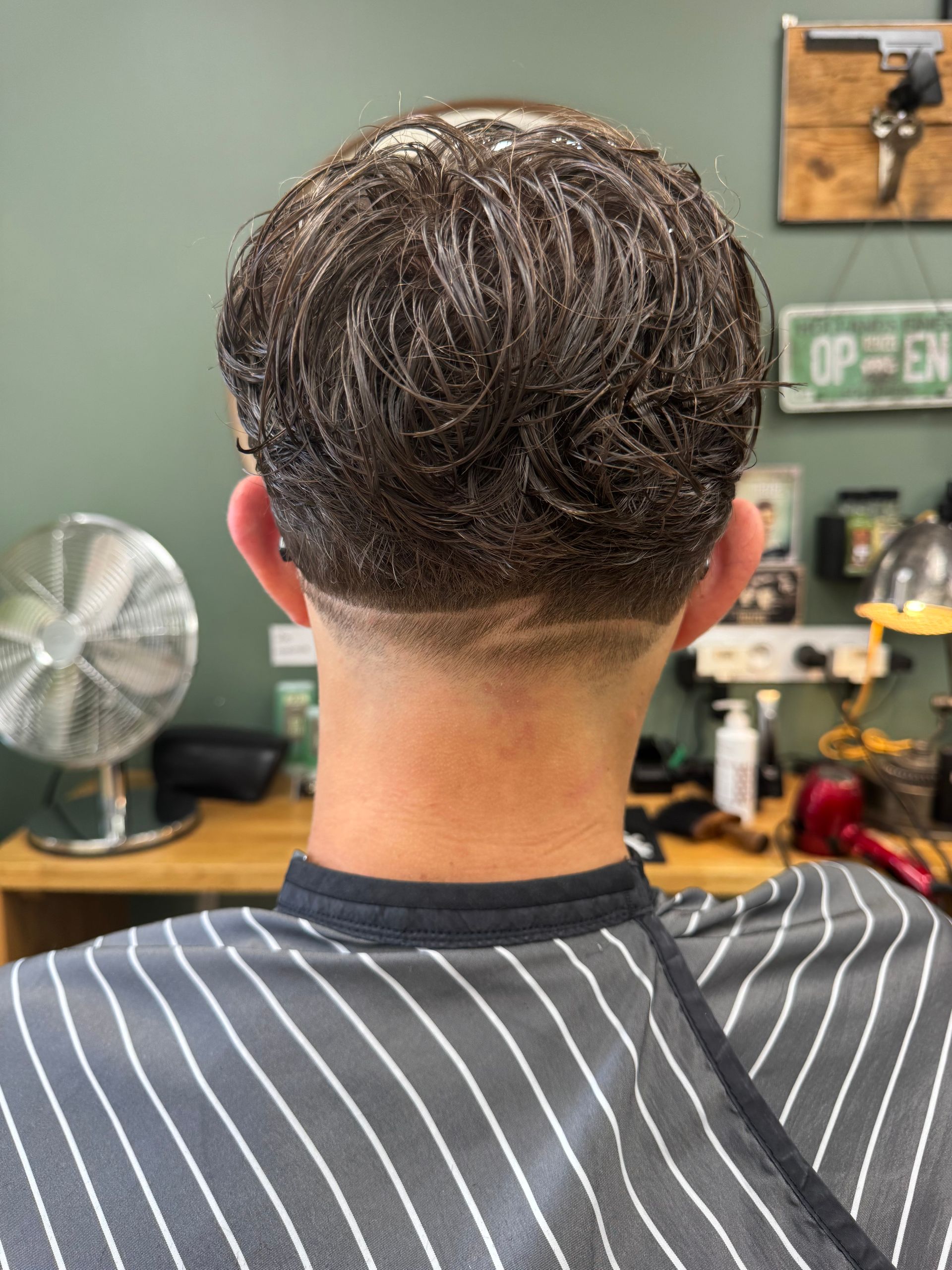 Dos d'une personne aux cheveux courts dégradés, dans un salon de coiffure
