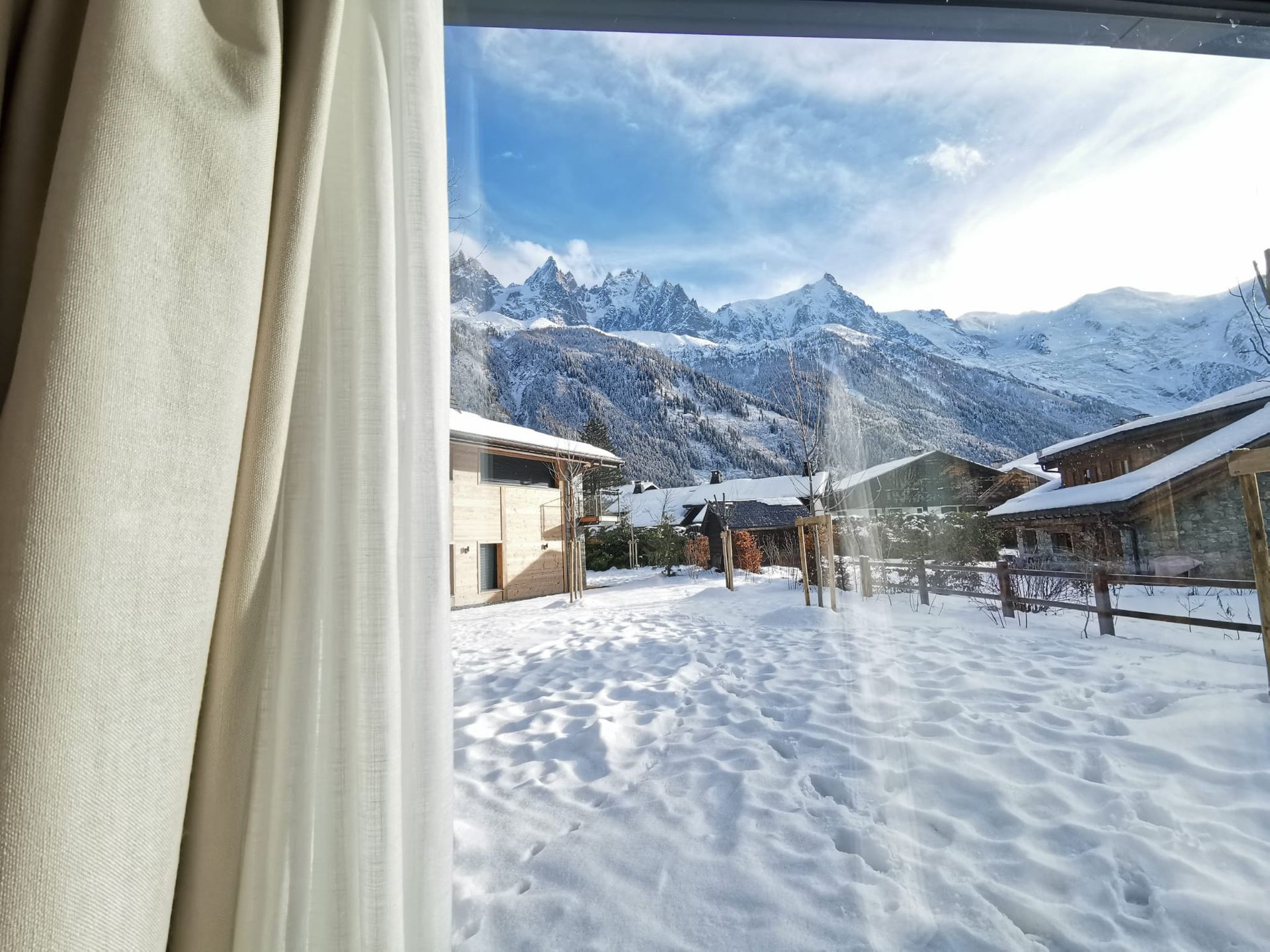 Vue sur un jardin enneigé et des chalets de montagne avec panorama sur les sommets alpins enneigés.