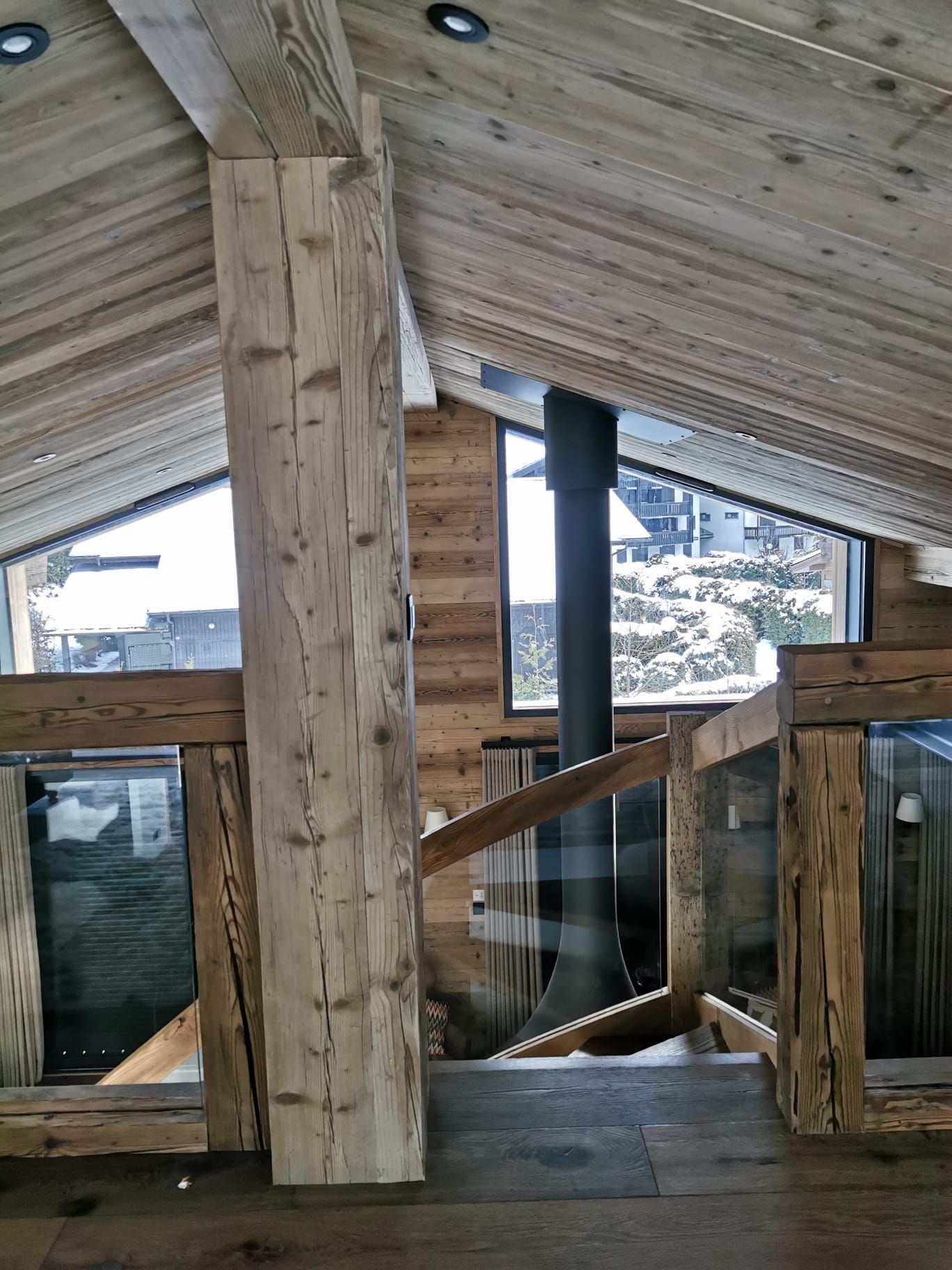 Intérieur chaleureux d’un chalet de montagne en bois avec grandes baies vitrées et vue sur un paysage enneigé.