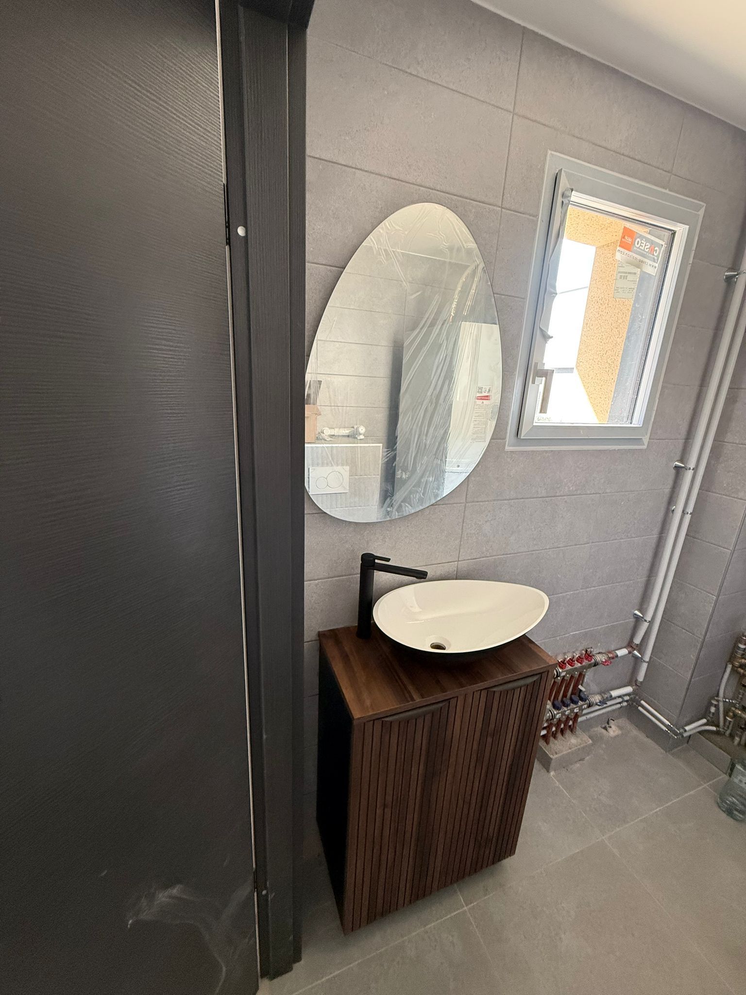 Salle de bains contemporaine avec meuble vasque en bois, miroir ovale et finitions modernes dans des tons gris.