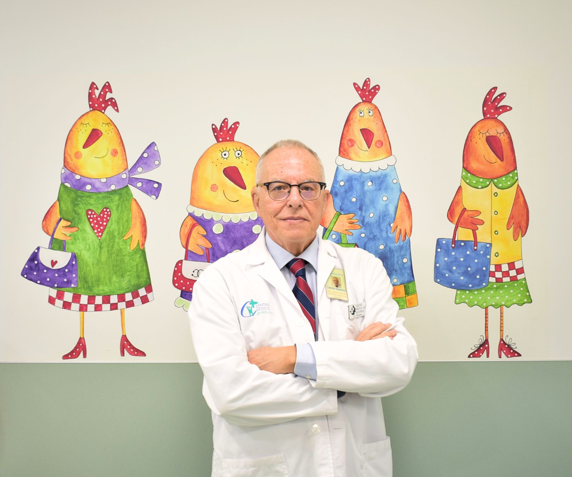 Médico con bata blanca sentado en un escritorio, mirando a la cámara.