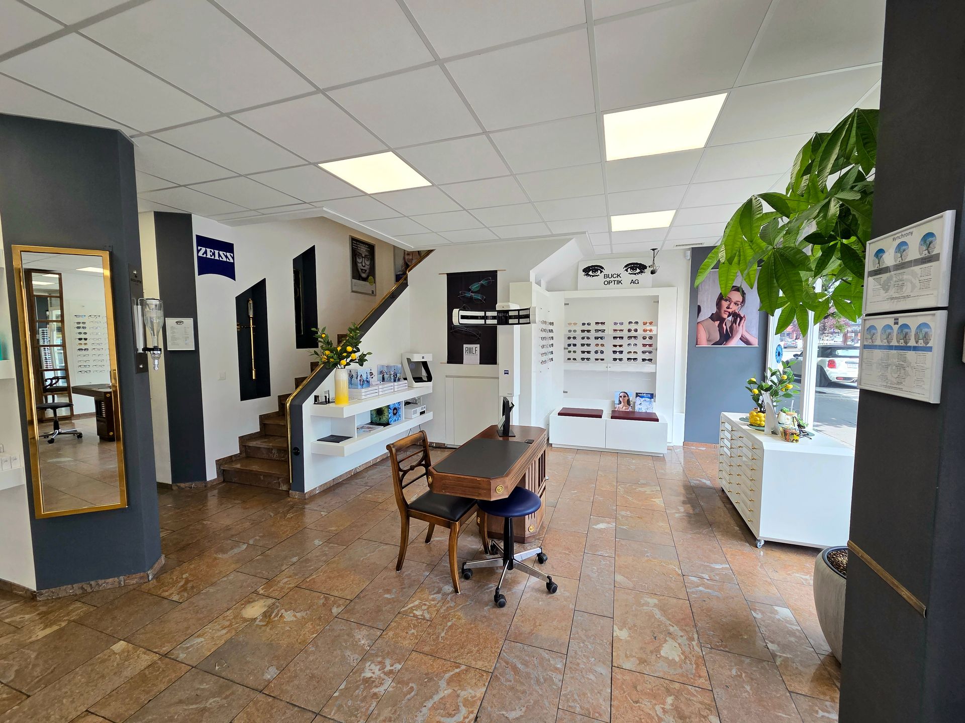 Innenansicht eines Optikergeschäfts mit Brillenauslagen, einer Treppe und einem Beratungsschalter.
