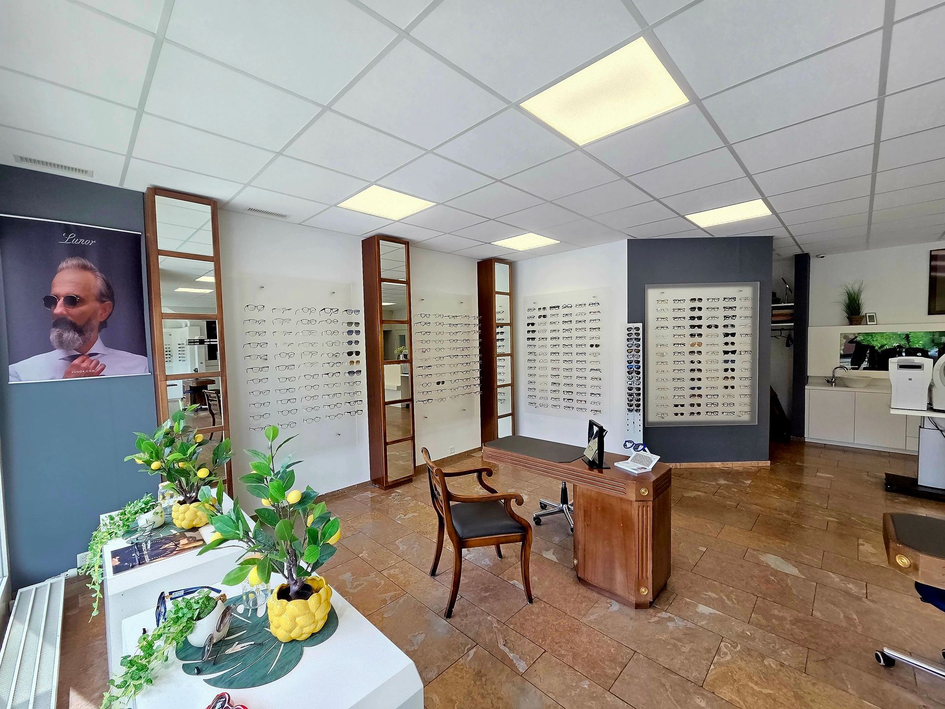 Inneneinrichtung eines Optikergeschäfts mit Brillendisplays, Schreibtisch und einem Porträt an der Wand.